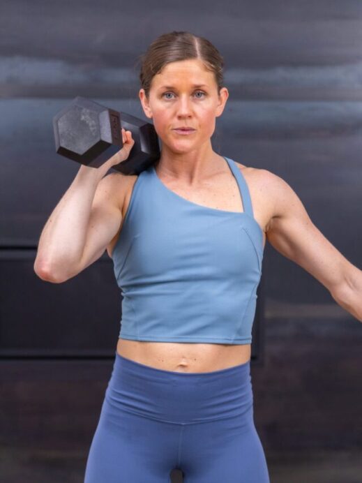 woman holding a dumbbell at her shoulder in an arm workout routine